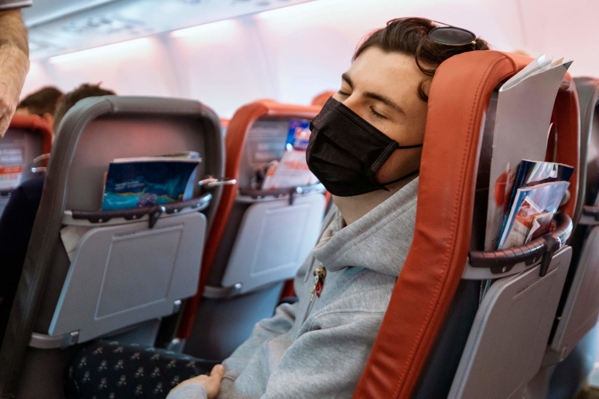 Ein Mann, der eine Gesichtsmaske trägt, während er in einem Flugzeug sitzt.