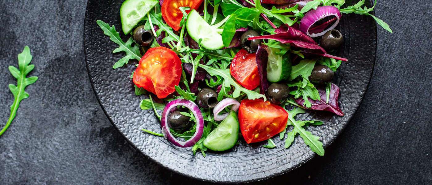 ein Salat mit Tomaten, Kopfsalat und Oliven auf einem Teller.